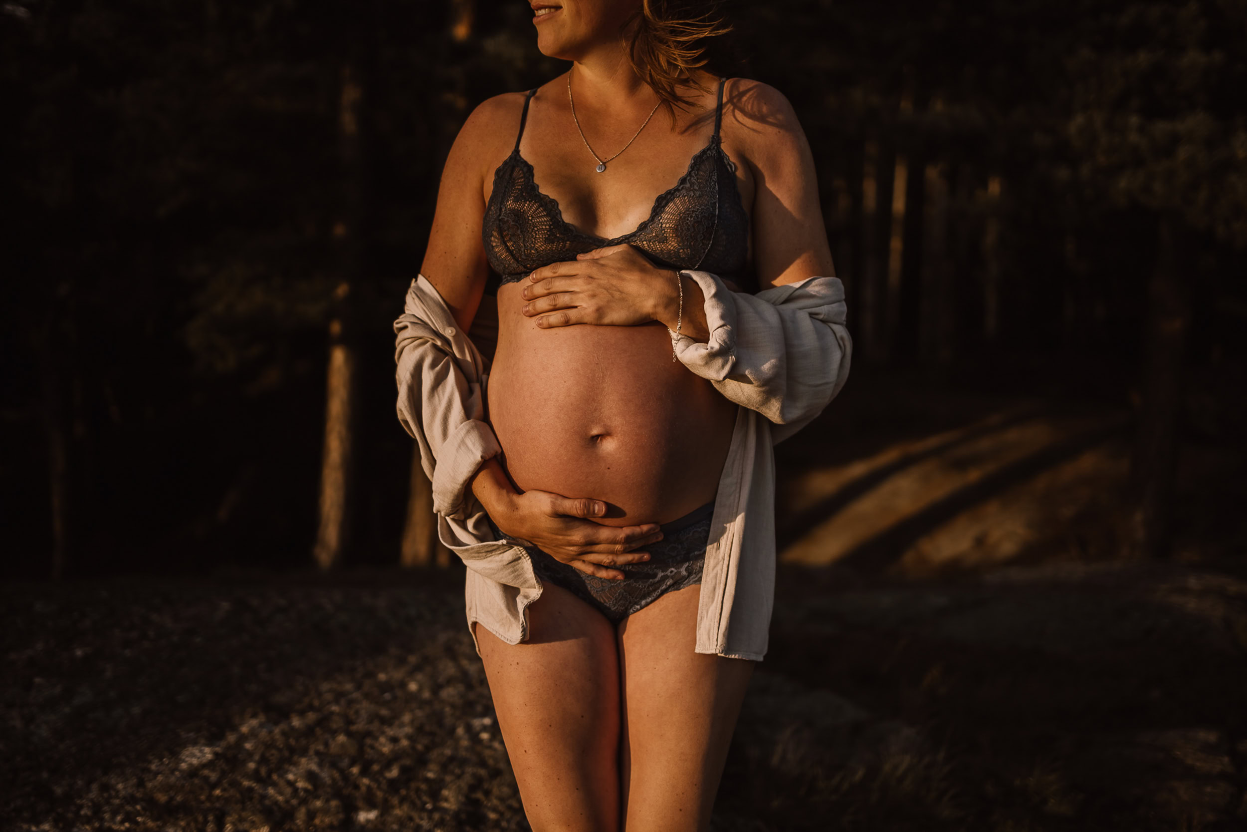 Gravid kvinna håller sig om magen och tittar bortåt under golden hour.