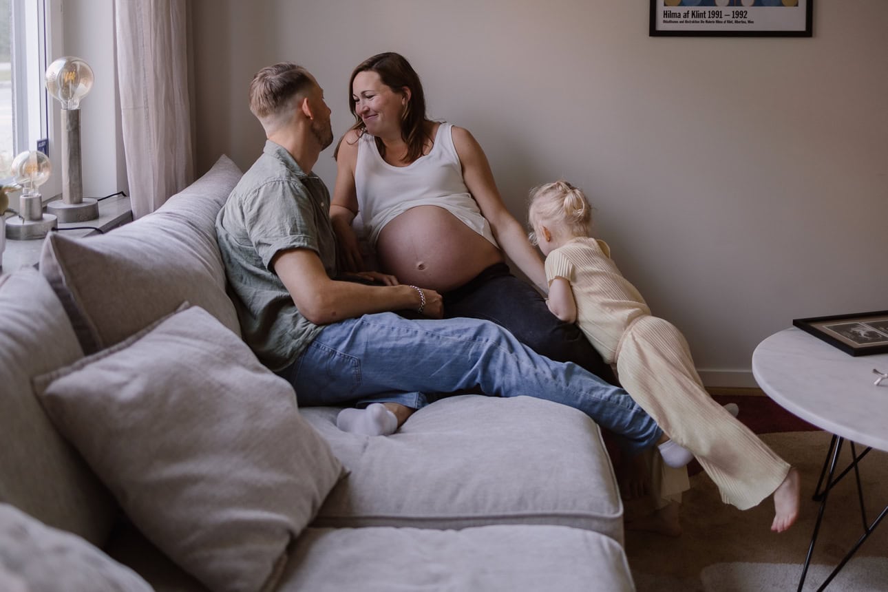 Gravid kvinna sitter i soffan tillsammans med sin familj.