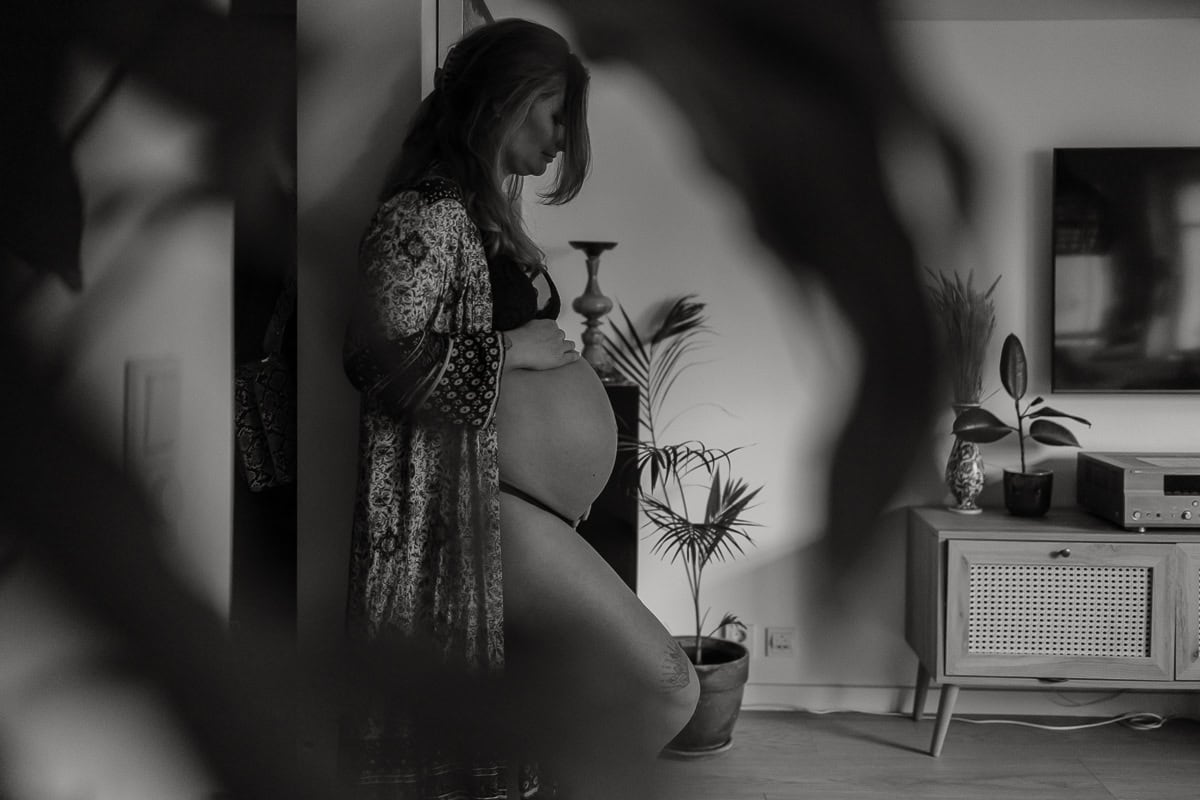 Gravid kvinna står mot en vägg och tittar ned på sin mage.