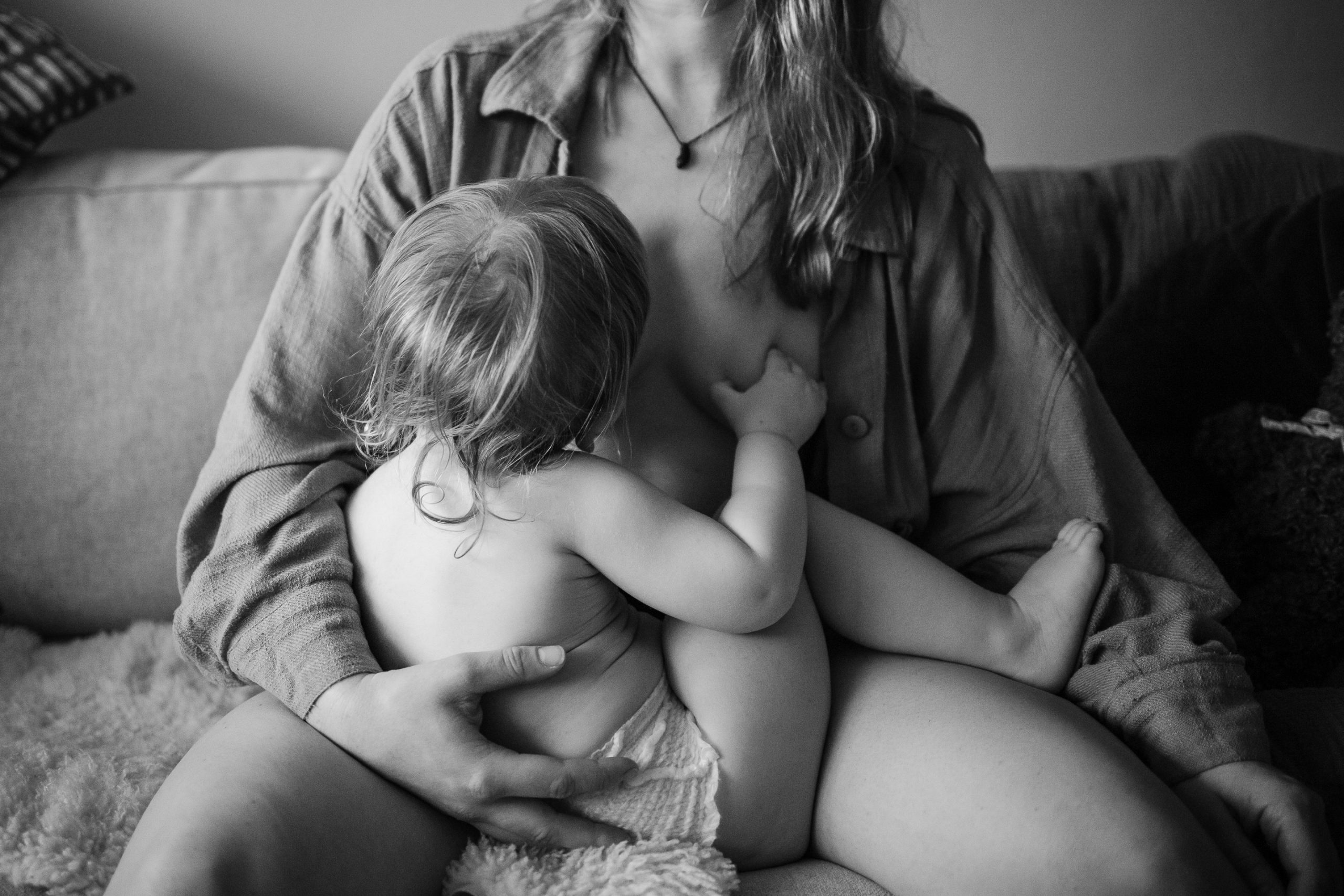 En mamma sitter i soffan och ammar sitt barn.